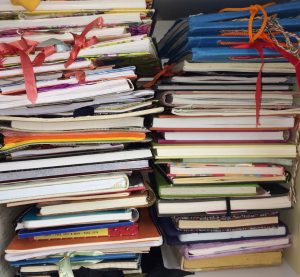 Two stacks of store-bought and handmade journals, approximately 47 journals in total. Journals and image by Mona Benjamintz.